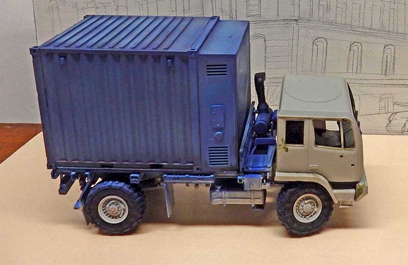 Maquette de camion militaire avec conteneur bleu vu de profil devant un décor urbain
