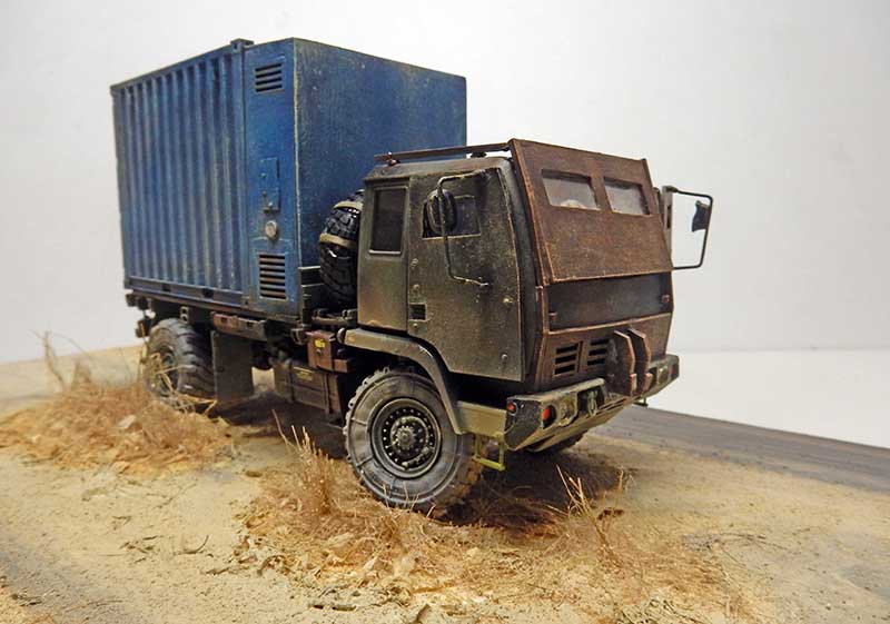 Maquette de camion militaire blindé avec conteneur bleu sur diorama de terrain aride