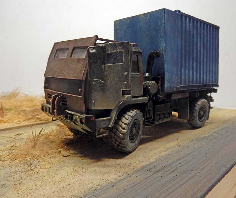 Maquette de camion militaire blindé avec conteneur bleu vieilli sur diorama de route abandonnée