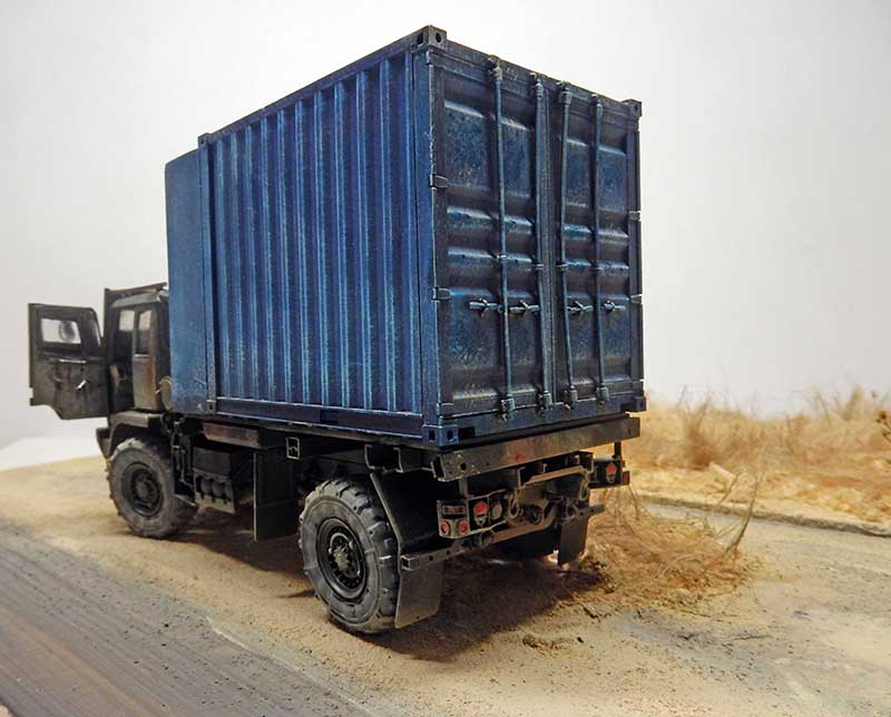 Maquette de camion militaire transportant un conteneur bleu sur un diorama de terrain désertique