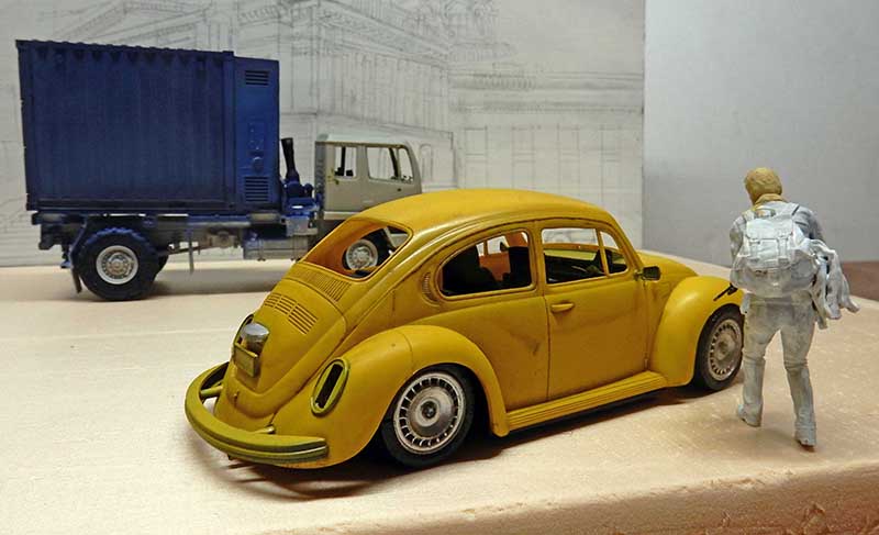 Maquette de Coccinelle jaune vieillie avec figurine au sac à dos et camion en arrière-plan
