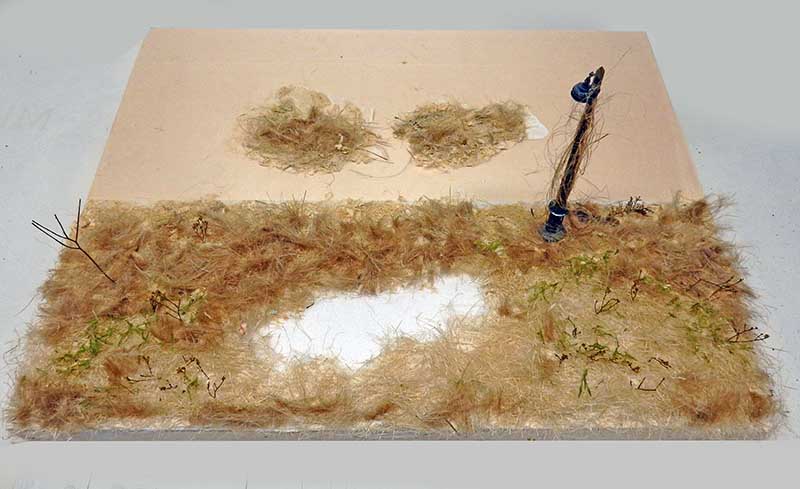 Diorama de maquettisme en construction avec végétation sèche, poteau et touffes d'herbe collées