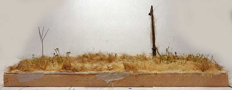 Diorama de maquettisme avec herbes sèches, broussailles et poteau en bois sur socle