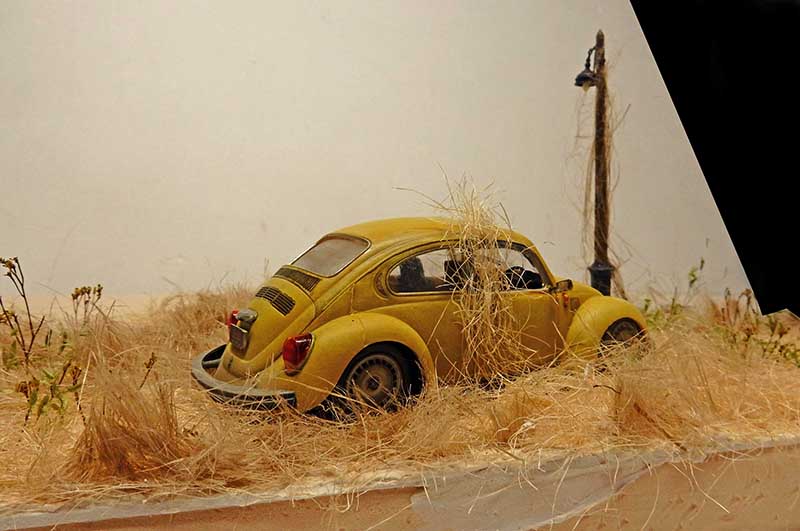 Maquette d'une Coccinelle Volkswagen jaune abandonnée dans les herbes sèches près d'un lampadaire