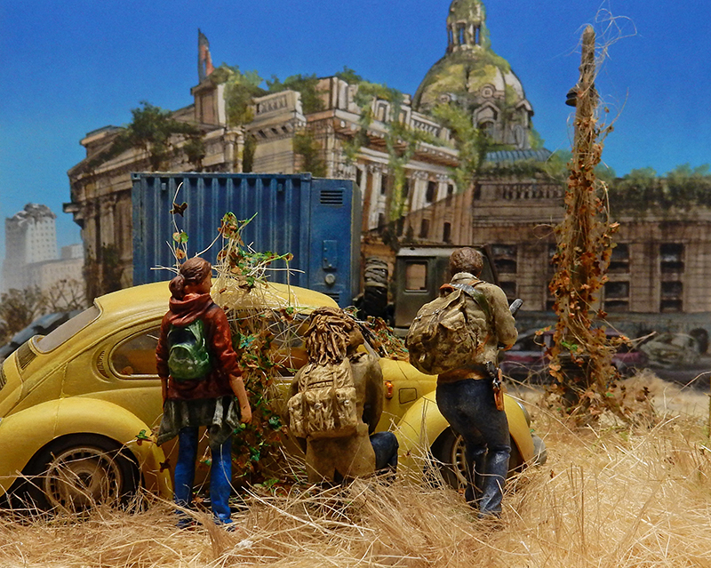 Diorama post-apocalyptique avec deux figurines près d'une coccinelle jaune envahie de végétation devant des ruines
