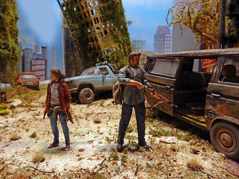 Diorama The Last of Us avec figurines de Joel armé et Ellie dans une ville post-apocalyptique en ruine