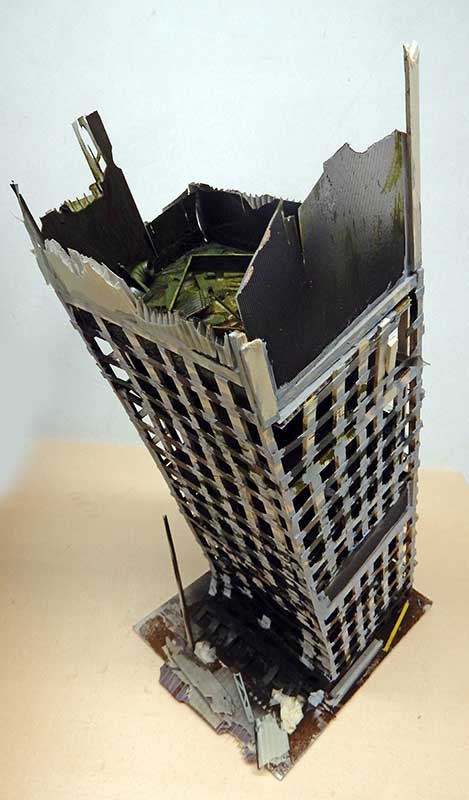 Maquette d'un gratte-ciel en ruine à structure exposée, façade détruite et débris à la base