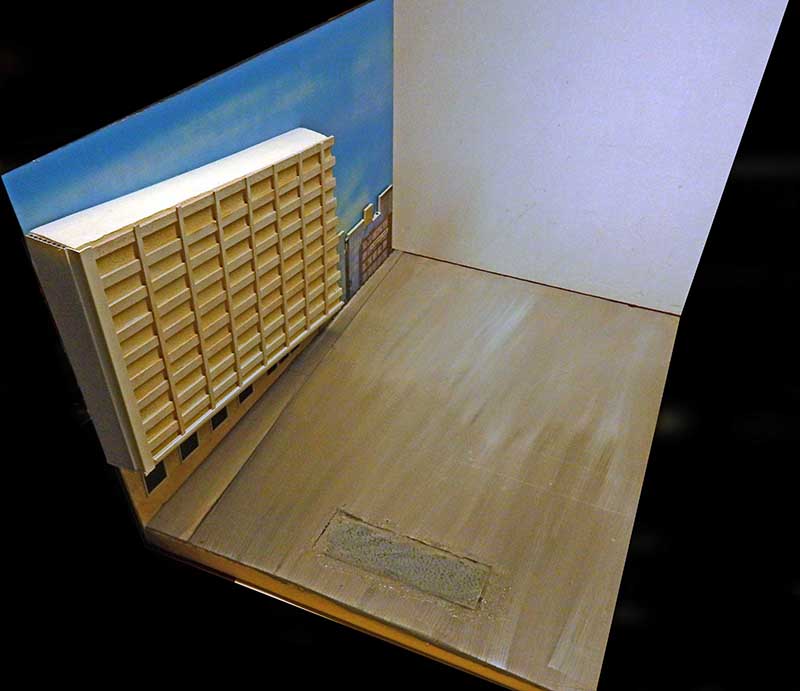 Diorama en construction avec immeuble en carton, sol en bois et fond de ciel peint
