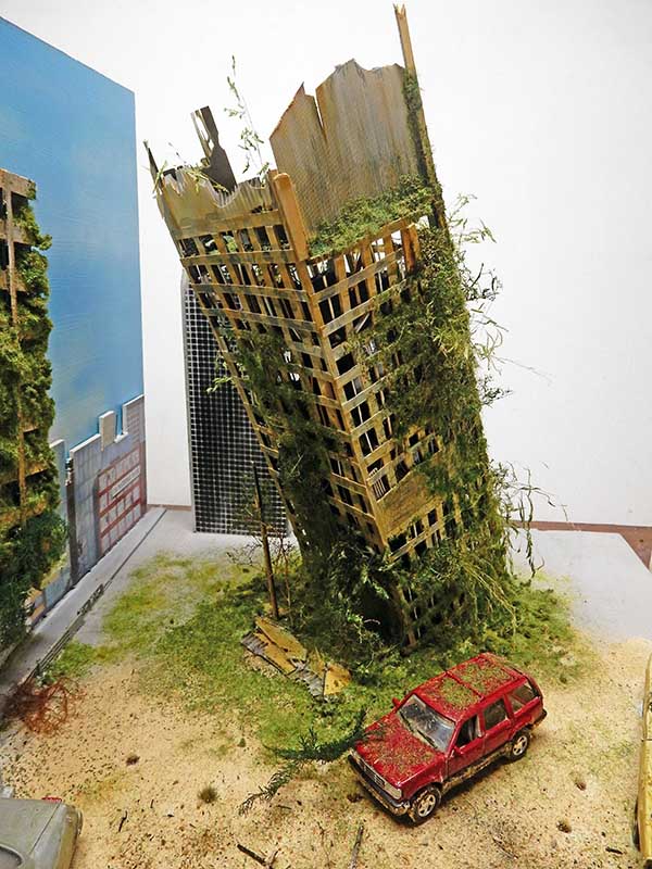 Maquette de bâtiment en ruine envahi par la végétation avec voiture rouge abandonnée