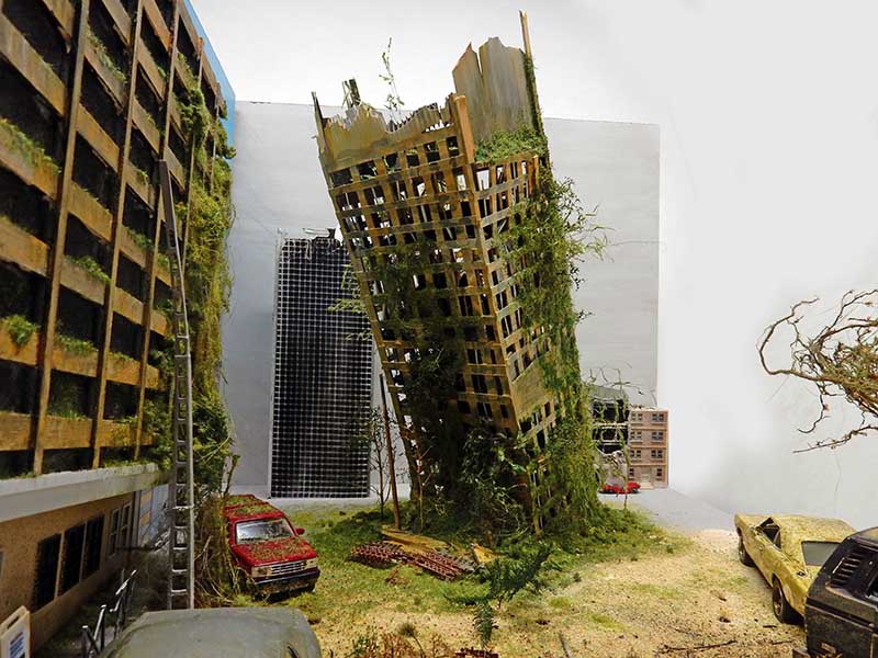 Maquette de ville post-apocalyptique avec gratte-ciel effondré envahi de végétation, immeubles et voitures rouillées
