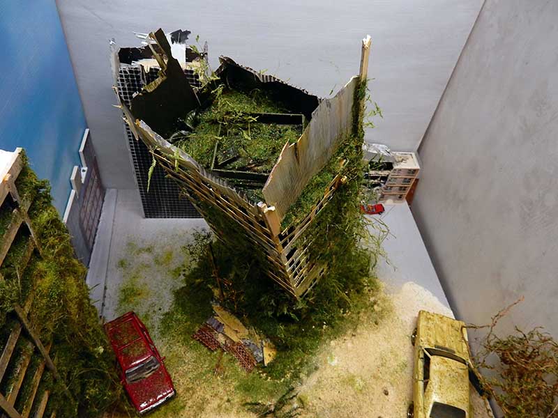 Maquette d'immeuble en ruine envahi de végétation avec voitures abandonnées vues de dessus