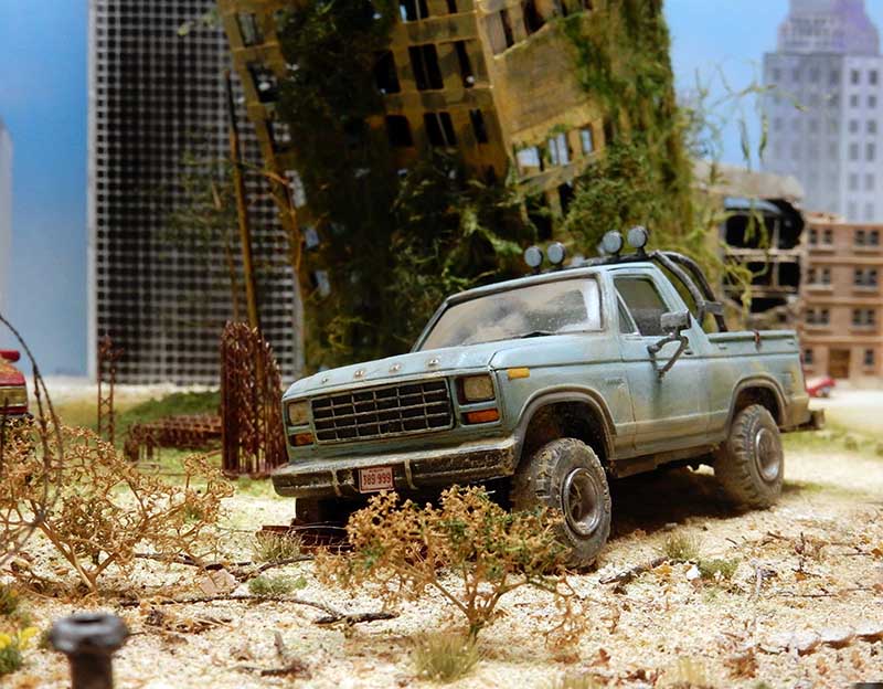 Maquette de pick-up Ford vieilli dans un diorama urbain post-apocalyptique avec immeubles en ruine