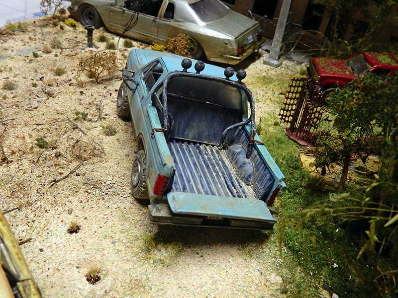Pick-up bleu rouillé maquette abandonné dans diorama post-apocalyptique sablonneux avec véhicule et végétation