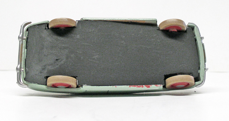 Dessous d'une maquette de voiture verte montrant châssis gris, roues beige et jantes rouges