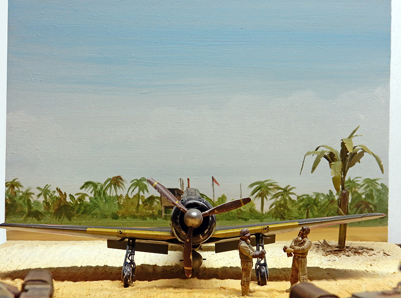 Maquette d'avion japonais vue de face dans un diorama tropical avec deux figurines de mécaniciens et palmiers