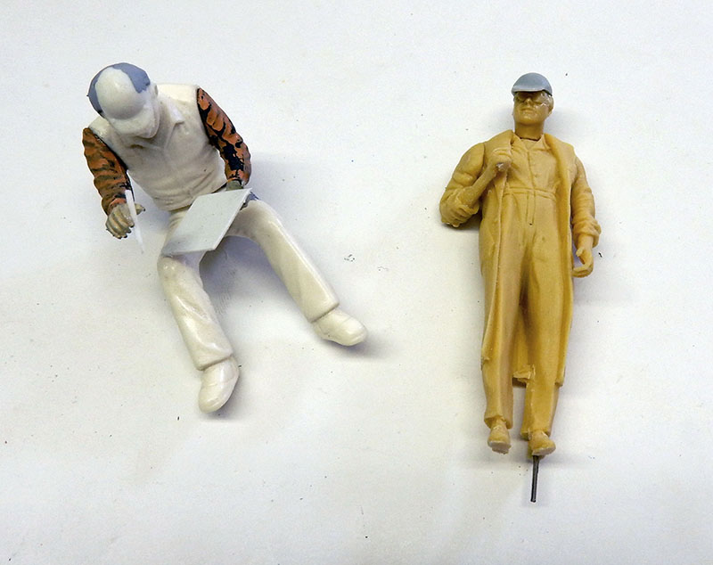 Deux figurines de personnages à l'échelle 1/24, l'une peinte assise, l'autre en résine brute