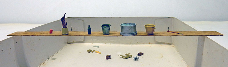 Étagère miniature avec pots de peinture et pinceaux sur planche en bois au-dessus d'un atelier