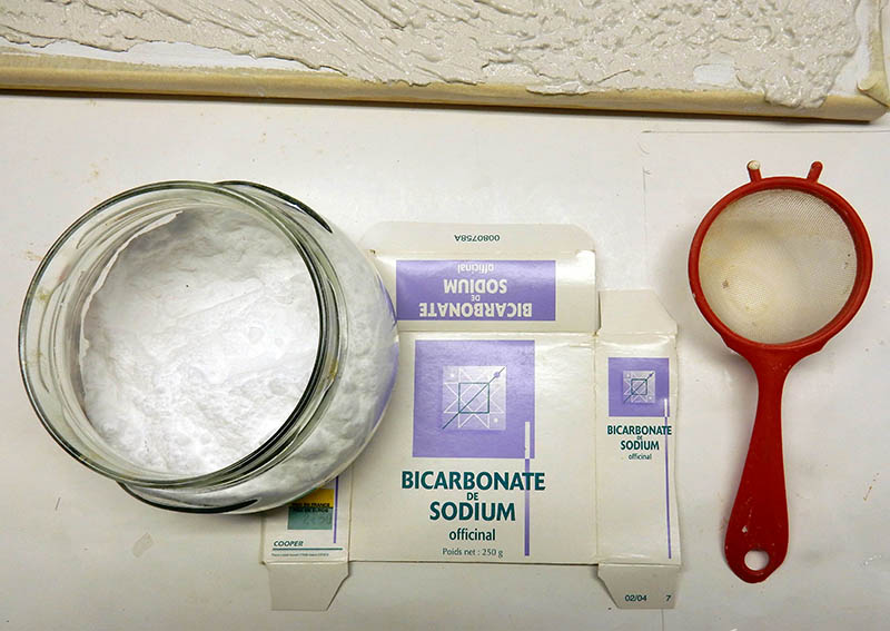 Bocal de bicarbonate de sodium, sa boîte et une passoire rouge pour saupoudrer la neige