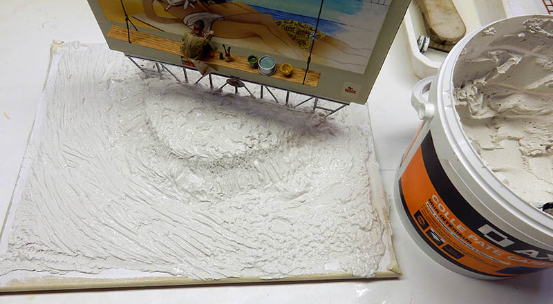 Modelage du relief de plage à la pâte blanche sur socle de diorama, pot de colle à côté