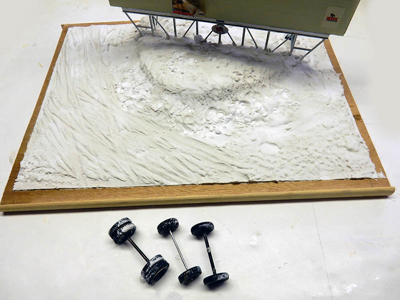 Diorama de socle enneigé en construction avec essieux et roues de maquette au premier plan
