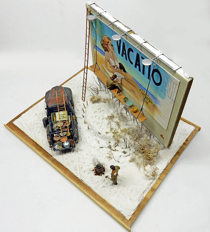 Diorama de maquettisme avec camion-citerne rouillé peignant un panneau publicitaire Vacation dans un décor désertique enneigé