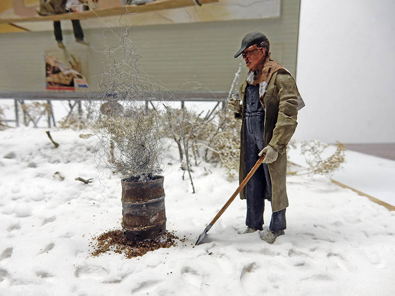 Figurine d'homme avec pelle près d'un bidon fumant dans un décor enneigé