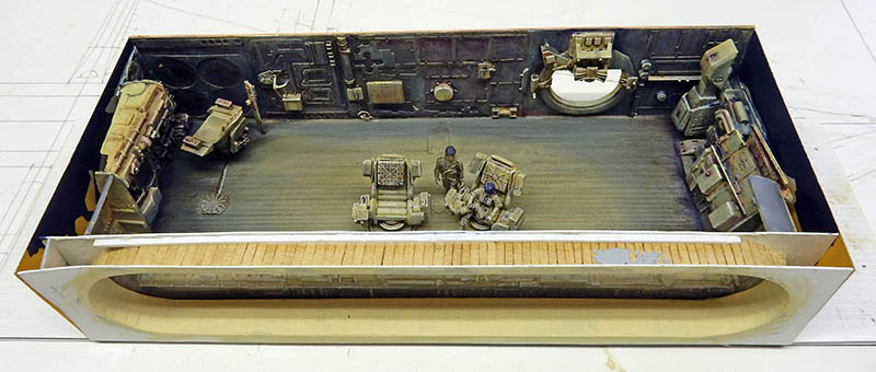Diorama du hangar de l'astronef Valérian, véhicules, caisses et figurines sur plancher métallique