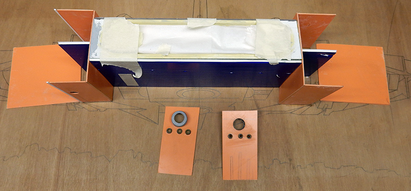 Fuselage de l'astronef en montage avec ailerons orange et panneaux détaillés sur plan