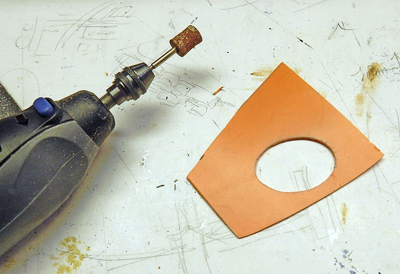 Outil rotatif et pièce de plastique orange percée d'une ouverture ovale sur l'établi