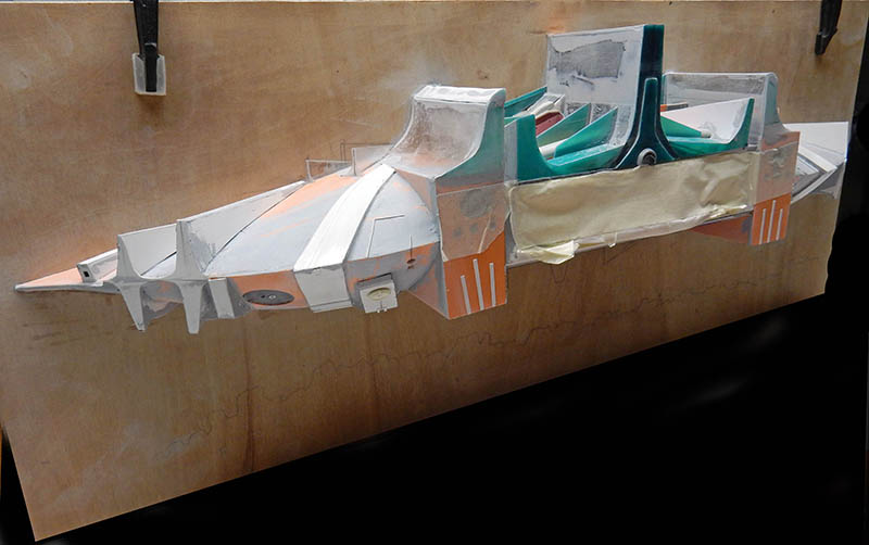 Fuselage de l'astronef en cours de montage devant le plan, panneaux blancs orange et verts