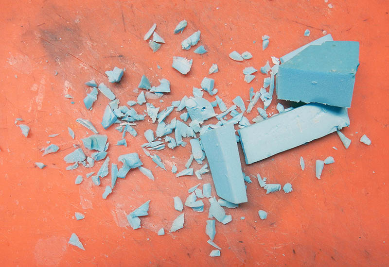 Chutes et copeaux de mousse polystyrène bleue découpée sur un tapis de coupe orange