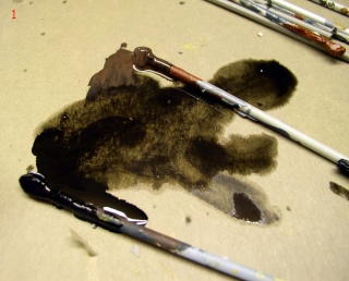 Pinceaux et jus de peinture brun foncé étalés sur une palette de carton