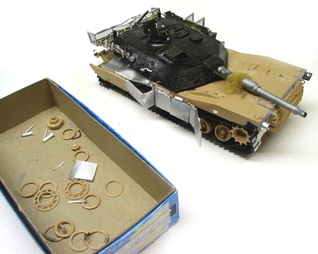 Maquette de char Abrams en cours de peinture sable à côté d'une boîte de pièces détachées