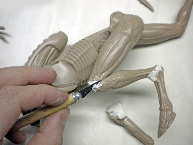 Application de mastic au couteau sur les jambes de la maquette Alien 3 en cours d'assemblage