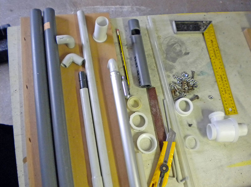 Tubes PVC, raccords, vis et outils de découpe disposés sur un établi de maquettisme