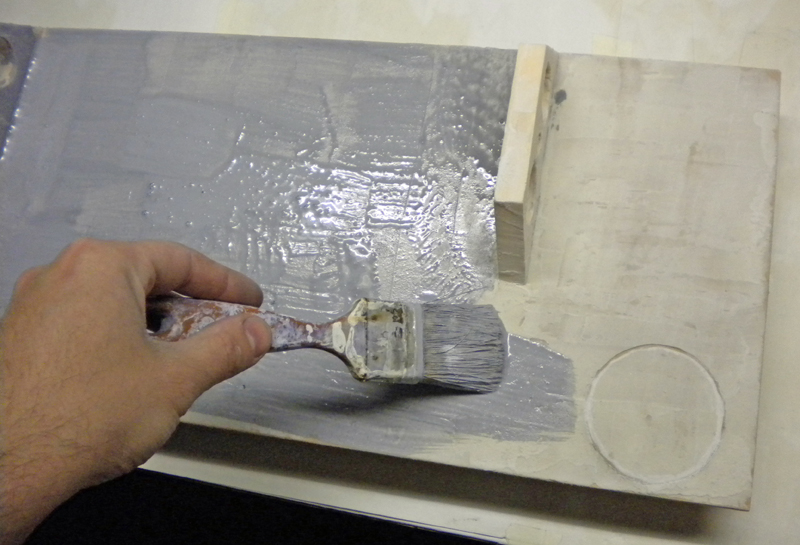 Application au pinceau d'une peinture grise sur un décor de maquette en plâtre
