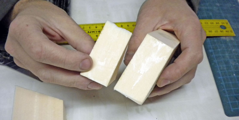 Mains tenant deux blocs de mousse découpés sur un plan de travail avec règle métallique