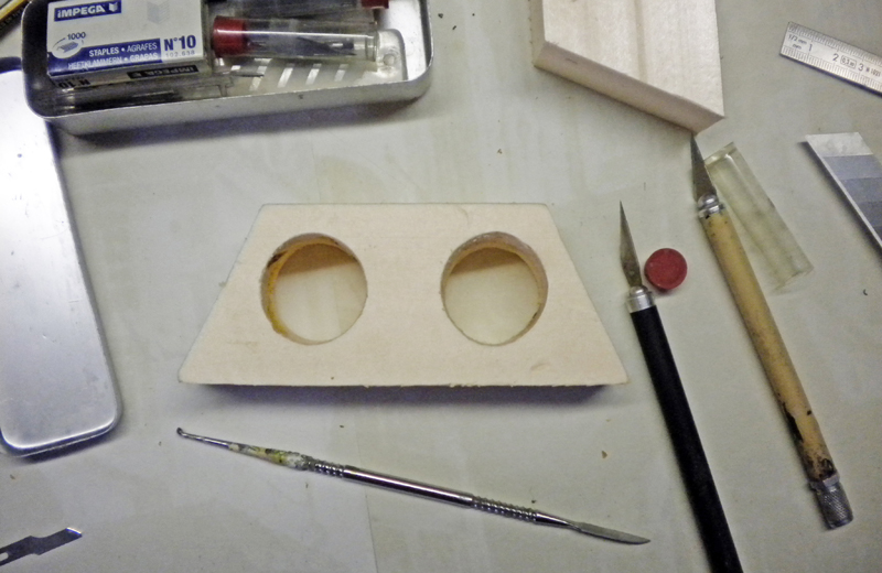 Plaque de bois percée de deux trous circulaires avec outils de modélisme sur l'établi