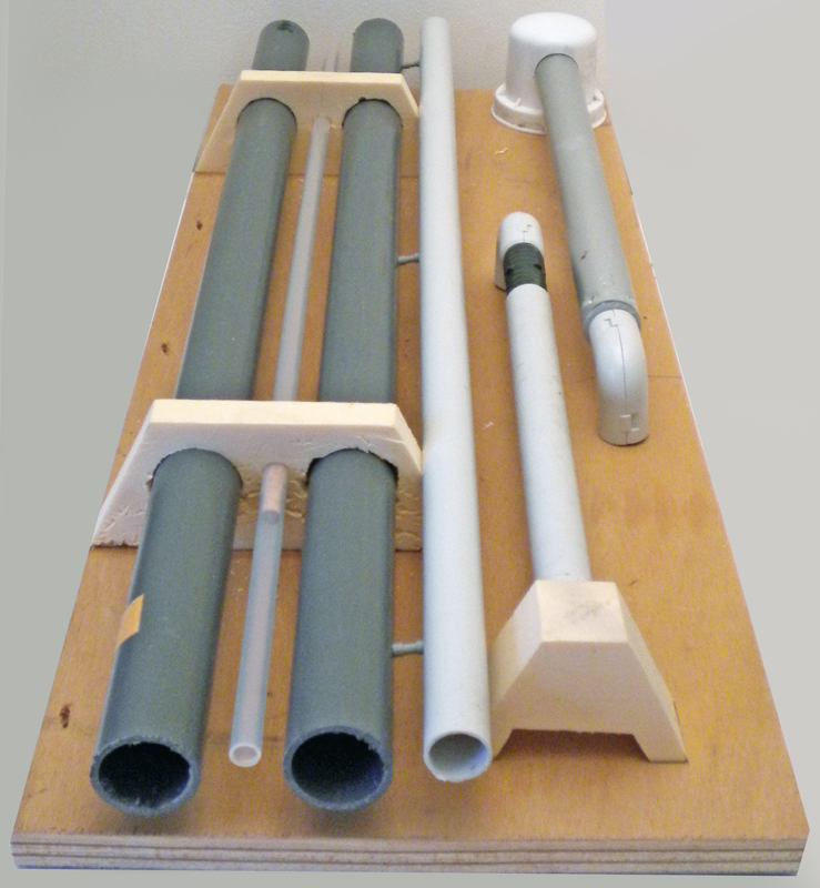 Tubes en PVC gris et blanc maintenus par supports en bois sur planche de montage