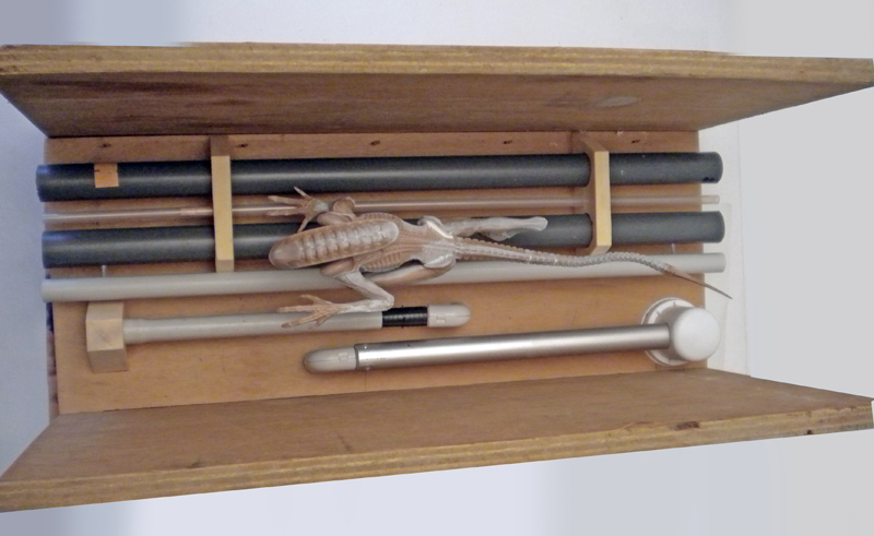 Figurine de xénomorphe quadrupède en cours de peinture posée dans une caisse en bois avec tubes