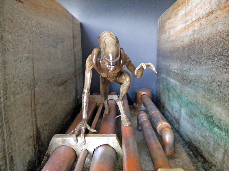 Maquette du xénomorphe d'Alien 3 accroupi sur des canalisations rouillées dans un couloir industriel