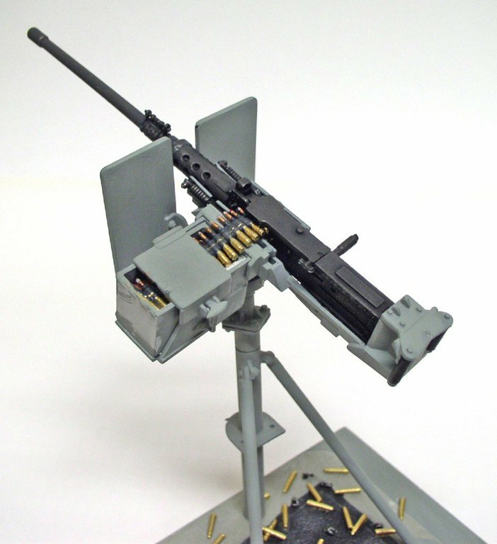 Mitrailleuse Browning M2 sur trépied, bande de munitions engagée, douilles éparpillées au sol