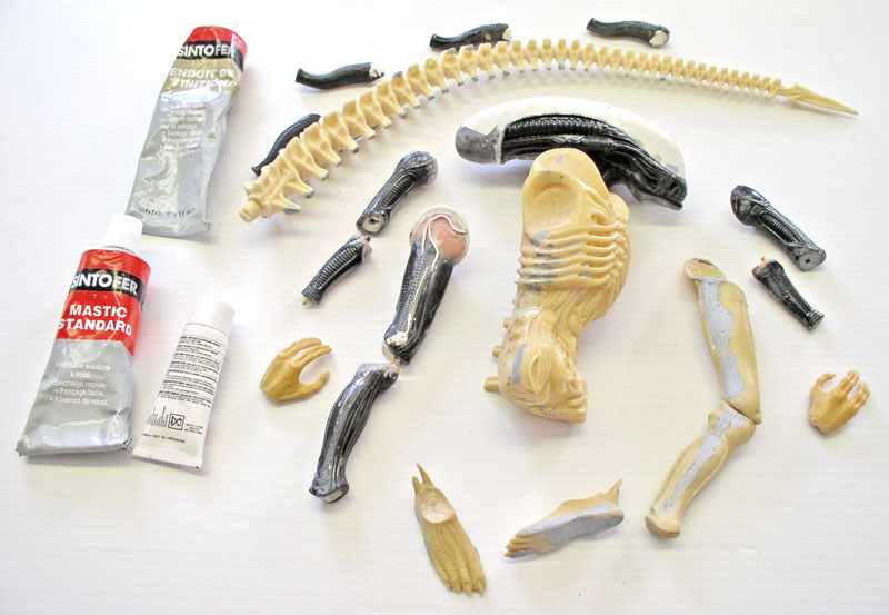 Pièces détachées d'une maquette d'Aqualien et tubes de mastic Sintofer sur fond blanc