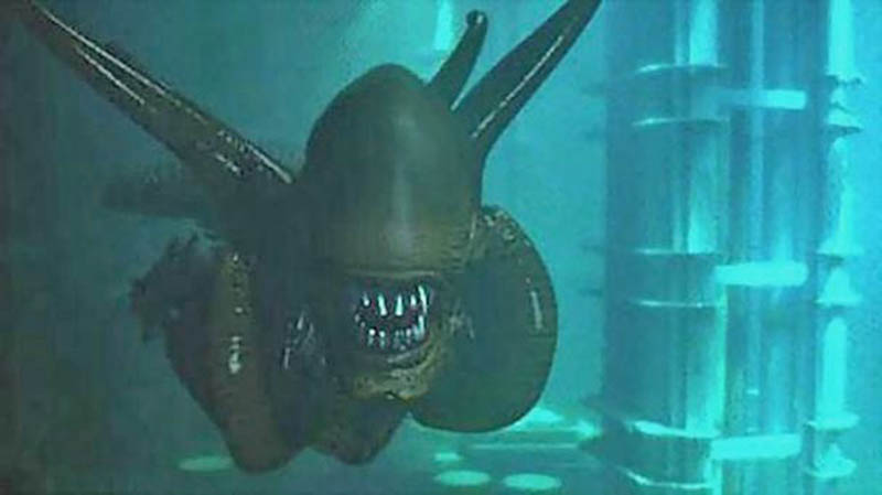 Maquette de créature Aqualien aux dents acérées immergée dans un décor sous-marin verdâtre
