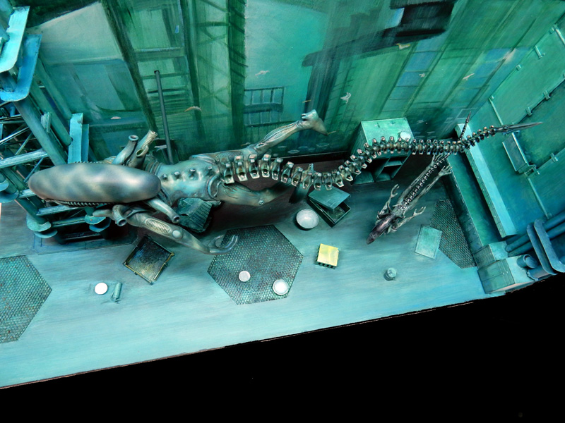 Maquette de créature aquatique extraterrestre à longue queue articulée dans un décor industriel sous-marin verdâtre