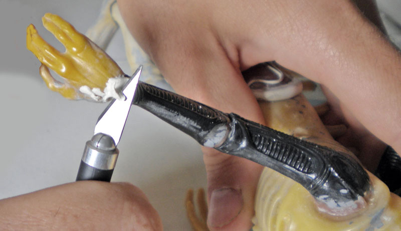 Application de mastic au cutter sur la main jaune d'une figurine Aqualien en cours de montage