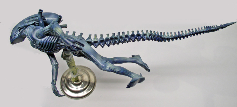 Maquette peinte de créature alien bleutée à longue queue segmentée, montée sur socle