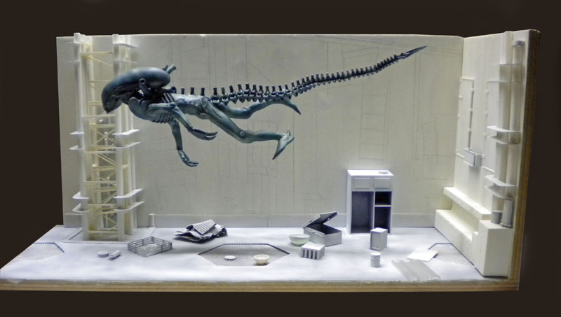 Diorama de maquette montrant une créature Aqualien suspendue au-dessus d'une salle technique aux parois blanches