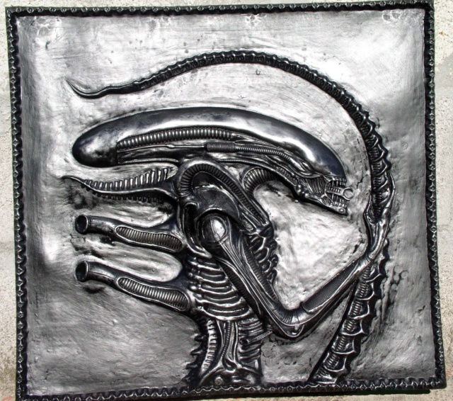 Bas-relief métallisé argenté représentant la tête et la main de l'Alien sur plaque encadrée