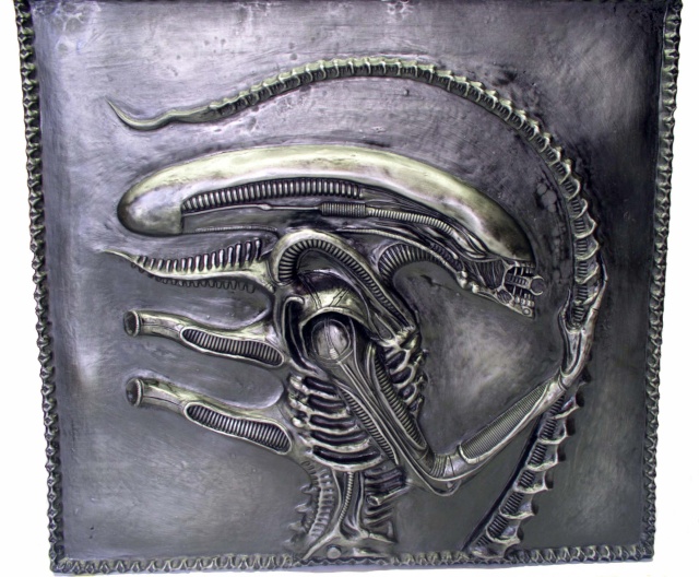 Bas relief patiné représentant la tête et le profil de l'Alien sur fond métallisé sombre